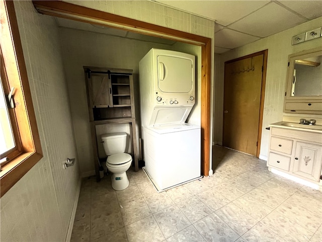 washroom with a barn door, stacked washer / dryer, sink, and light tile floors