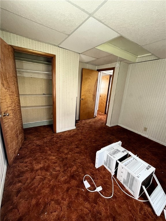 unfurnished bedroom with a closet, dark carpet, and a paneled ceiling