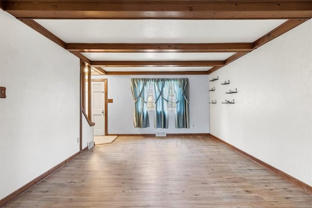 empty room featuring beamed ceiling and light wood-type flooring