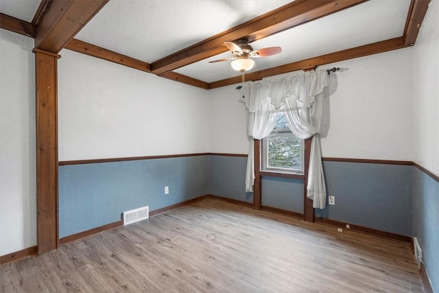 spare room featuring light hardwood / wood-style floors, ceiling fan, and beamed ceiling