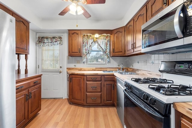 kitchen with ceiling fan, appliances with stainless steel finishes, light hardwood / wood-style floors, sink, and tasteful backsplash