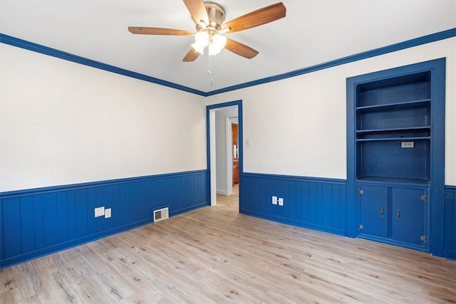 spare room with crown molding, built in features, light hardwood / wood-style floors, and ceiling fan