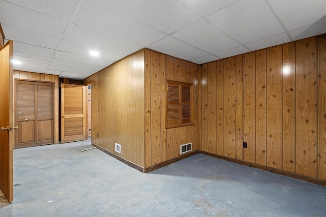 basement featuring a paneled ceiling and wood walls