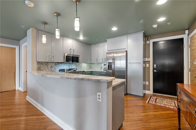 kitchen with light hardwood / wood-style floors, stainless steel appliances, kitchen peninsula, backsplash, and hanging light fixtures