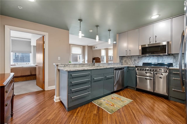 kitchen with gray cabinetry, stainless steel appliances, decorative light fixtures, and light wood-type flooring