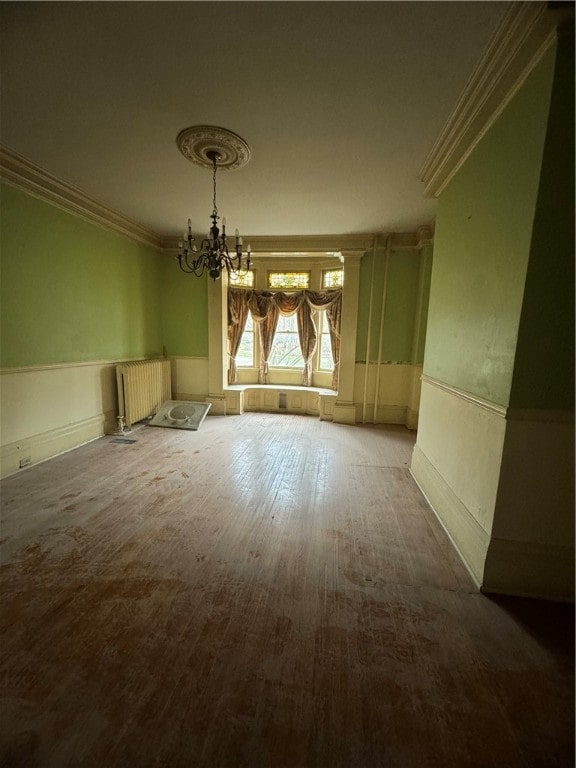 empty room featuring an inviting chandelier, hardwood / wood-style floors, radiator heating unit, and ornamental molding