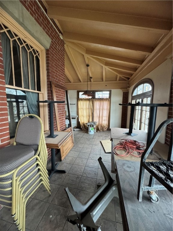 interior space featuring brick wall, dark tile flooring, and lofted ceiling with beams