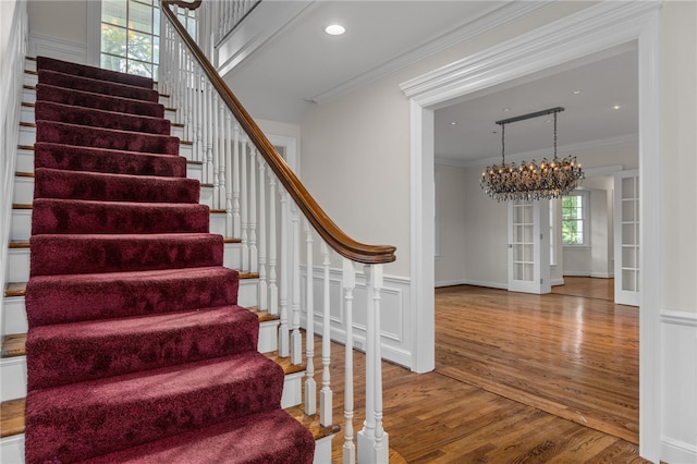 staircase featuring light hardwood / wood-style floors, ornamental molding, and a notable chandelier