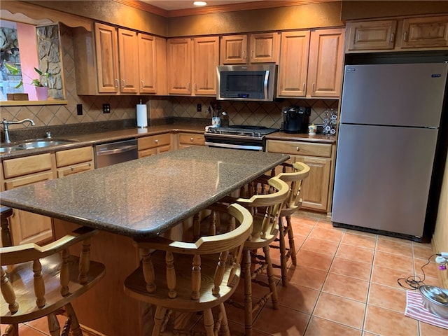 kitchen with sink, light tile floors, appliances with stainless steel finishes, a breakfast bar, and backsplash