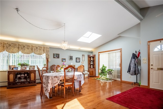 dining area featuring vaulted ceiling with skylight, a notable chandelier, a baseboard heating unit, and light hardwood / wood-style floors