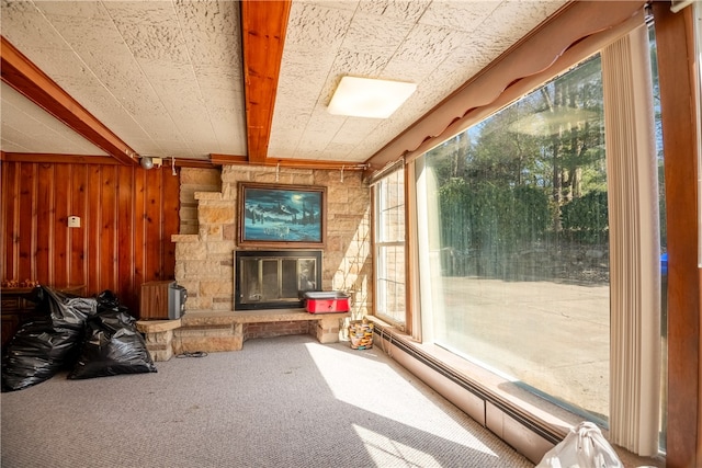 interior space featuring a baseboard heating unit, beamed ceiling, and a stone fireplace