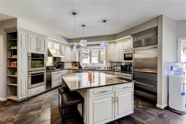 kitchen with hanging light fixtures, dark stone counters, a kitchen island, stainless steel appliances, and wall chimney exhaust hood