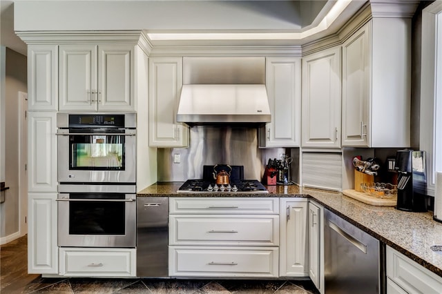 kitchen with dark stone counters, white cabinets, wall chimney range hood, and stainless steel appliances