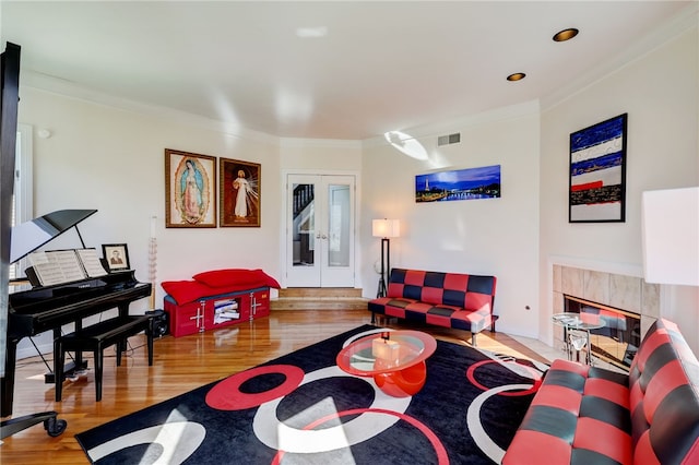 living room featuring ornamental molding, a tile fireplace, french doors, and light hardwood / wood-style flooring