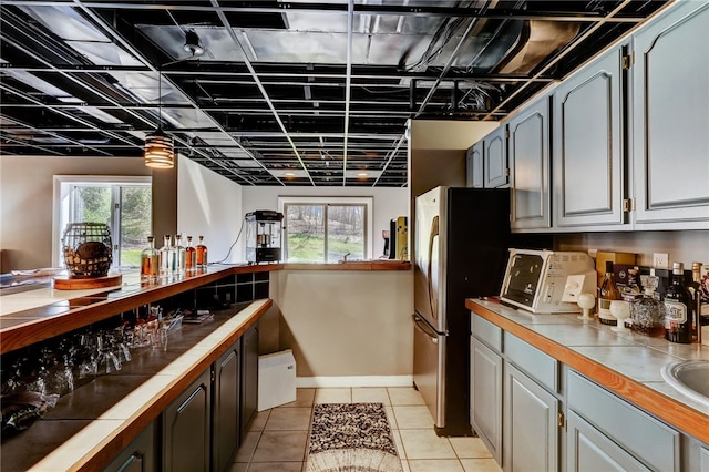 kitchen with stainless steel fridge, gray cabinets, a healthy amount of sunlight, and light tile floors