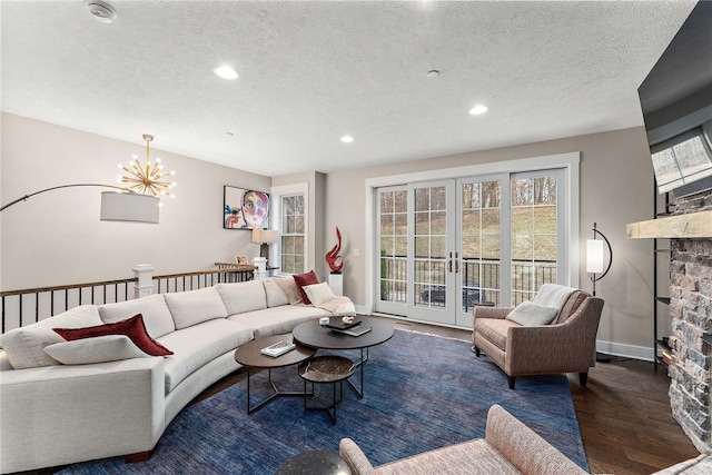 living room featuring a stone fireplace, a textured ceiling, a notable chandelier, dark hardwood / wood-style floors, and french doors