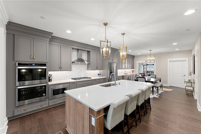 kitchen with wall chimney exhaust hood, sink, dark wood-type flooring, a center island with sink, and a kitchen breakfast bar