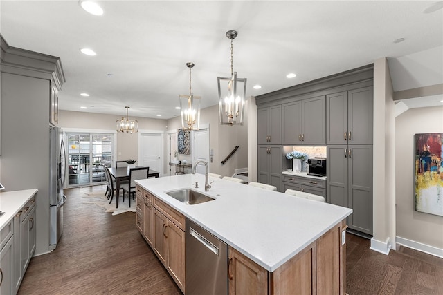 kitchen featuring decorative light fixtures, stainless steel appliances, a center island with sink, sink, and dark hardwood / wood-style flooring