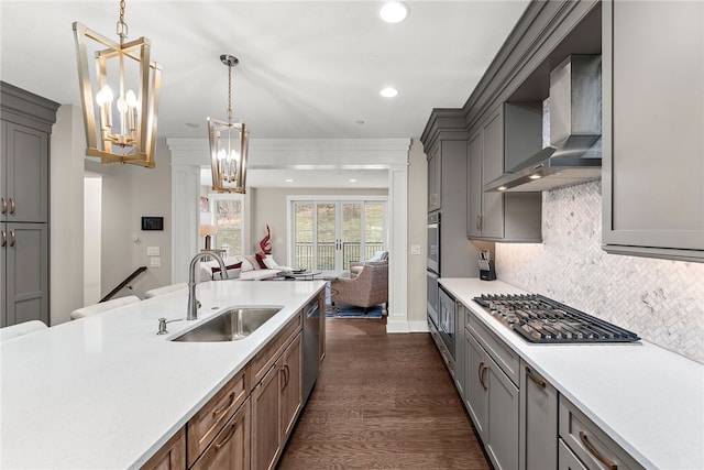 kitchen with wall chimney exhaust hood, hanging light fixtures, dark wood-type flooring, a notable chandelier, and tasteful backsplash