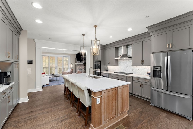 kitchen with wall chimney exhaust hood, a breakfast bar area, dark wood-type flooring, stainless steel appliances, and a kitchen island with sink