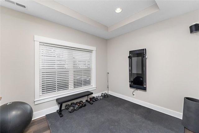 workout room featuring dark wood-type flooring and a tray ceiling