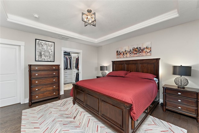 bedroom with a spacious closet, a raised ceiling, and dark wood-type flooring