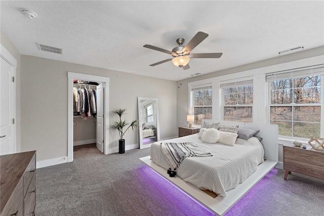 bedroom with dark colored carpet, a closet, ceiling fan, and a walk in closet