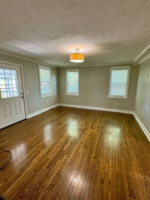 empty room featuring a textured ceiling, dark hardwood / wood-style floors, and ornamental molding