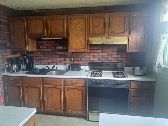 kitchen featuring range with gas stovetop, brick wall, a sink, light countertops, and under cabinet range hood