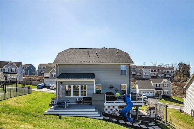 rear view of property featuring a garage, a wooden deck, and a lawn