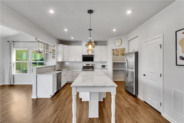 kitchen featuring a kitchen island, white cabinets, decorative light fixtures, stainless steel appliances, and wood-type flooring