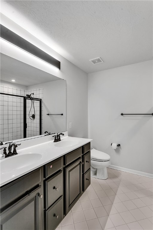 bathroom featuring dual bowl vanity, a shower with shower door, toilet, tile flooring, and a textured ceiling