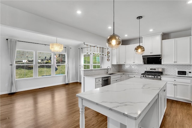 kitchen with white cabinets, dark hardwood / wood-style floors, appliances with stainless steel finishes, light stone counters, and a kitchen island