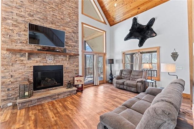 living room featuring high vaulted ceiling, light hardwood / wood-style floors, wooden ceiling, a stone fireplace, and french doors