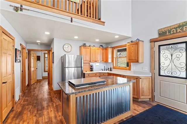 kitchen featuring stainless steel refrigerator, dark wood-type flooring, dark stone countertops, and a kitchen island