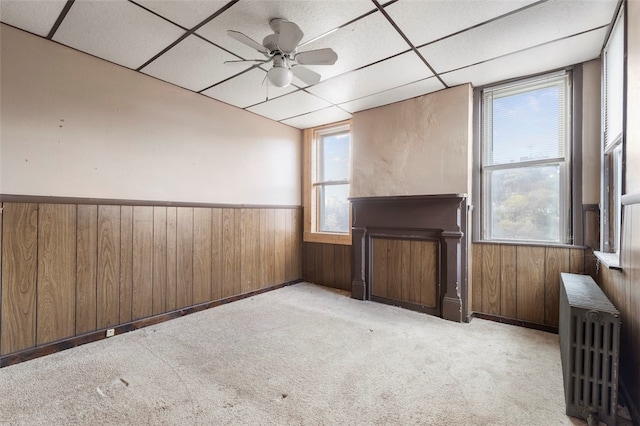 carpeted spare room with ceiling fan, radiator, and a drop ceiling