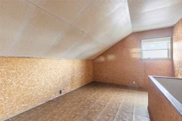 additional living space featuring parquet flooring, a textured ceiling, and vaulted ceiling