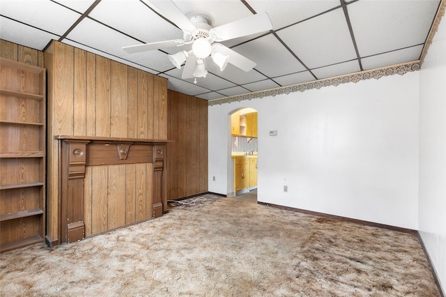 interior space featuring wood walls, a drop ceiling, light carpet, ensuite bathroom, and ceiling fan