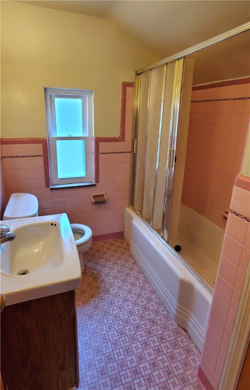 full bathroom featuring tile walls, vaulted ceiling, toilet, and vanity