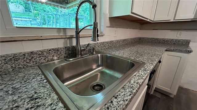 details with white cabinetry, stone counters, and sink