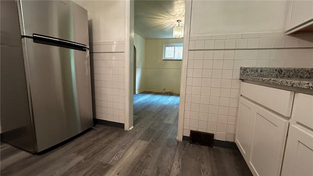 kitchen with stainless steel refrigerator, white cabinets, tile walls, and dark wood-type flooring