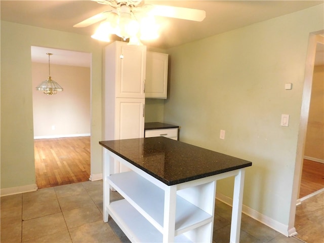 kitchen featuring pendant lighting, ceiling fan, white cabinets, dark stone countertops, and light tile flooring