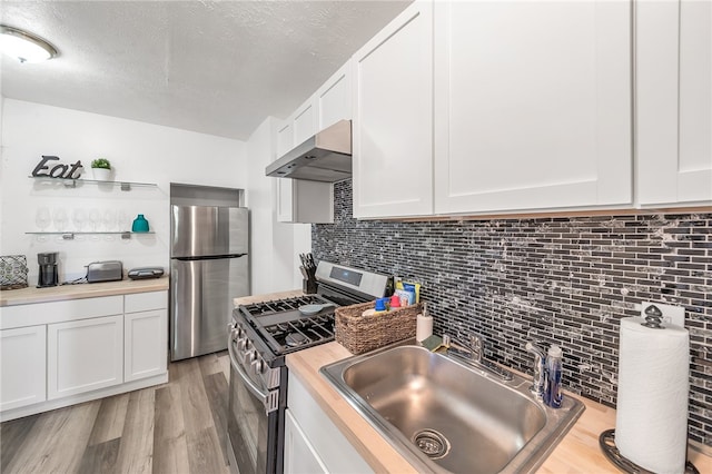 kitchen featuring appliances with stainless steel finishes, white cabinets, light wood-type flooring, wall chimney range hood, and sink