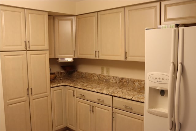 kitchen featuring white fridge with ice dispenser and light stone counters