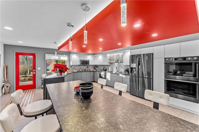 kitchen with hanging light fixtures, light hardwood / wood-style floors, gray cabinets, decorative backsplash, and appliances with stainless steel finishes