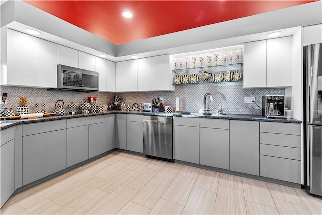 kitchen featuring gray cabinetry, sink, tasteful backsplash, dark stone countertops, and appliances with stainless steel finishes