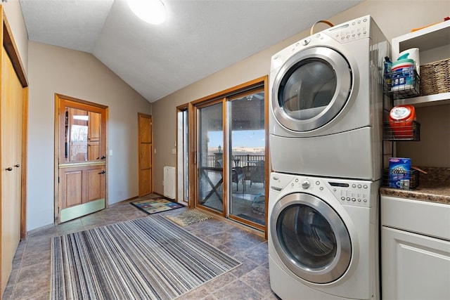 laundry area with dark tile floors, cabinets, and stacked washer and clothes dryer