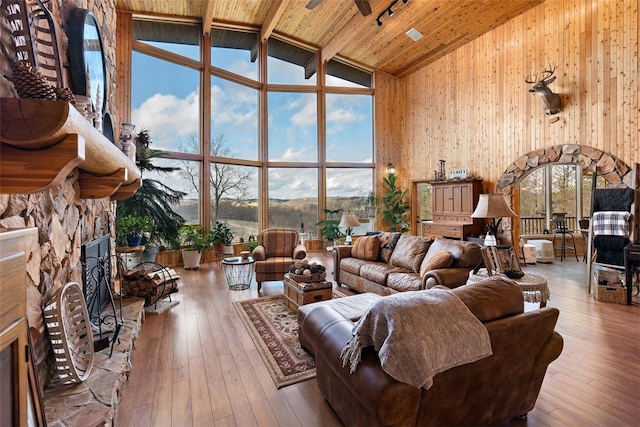 living room with wooden walls, high vaulted ceiling, light hardwood / wood-style flooring, wooden ceiling, and a stone fireplace