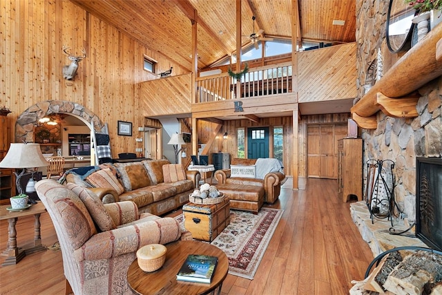 living room with a fireplace, high vaulted ceiling, light hardwood / wood-style flooring, and wooden walls