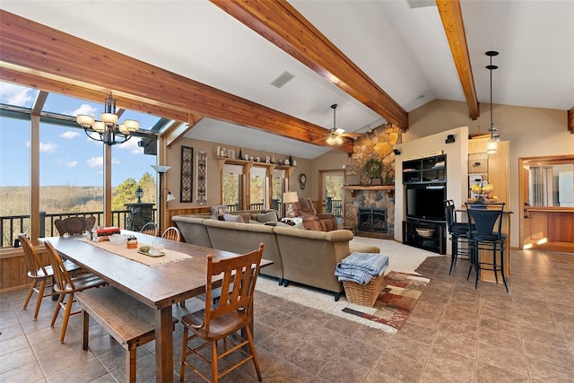 tiled dining area featuring ceiling fan with notable chandelier, vaulted ceiling with beams, and a stone fireplace